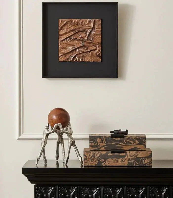 Decorative items on a black console table with a textured wall art piece above.