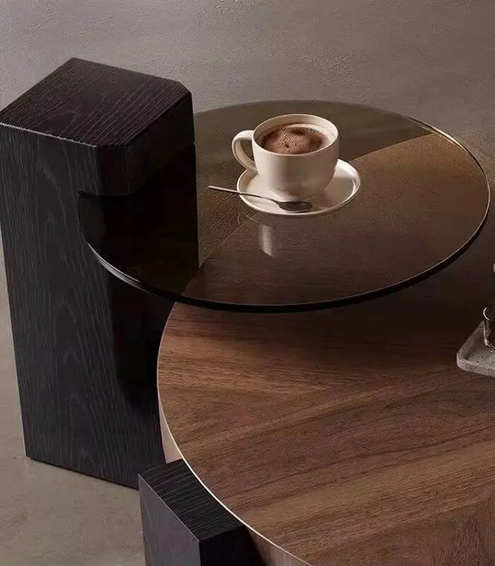 Modern round table with a glass top and wooden base, featuring a cup of coffee.