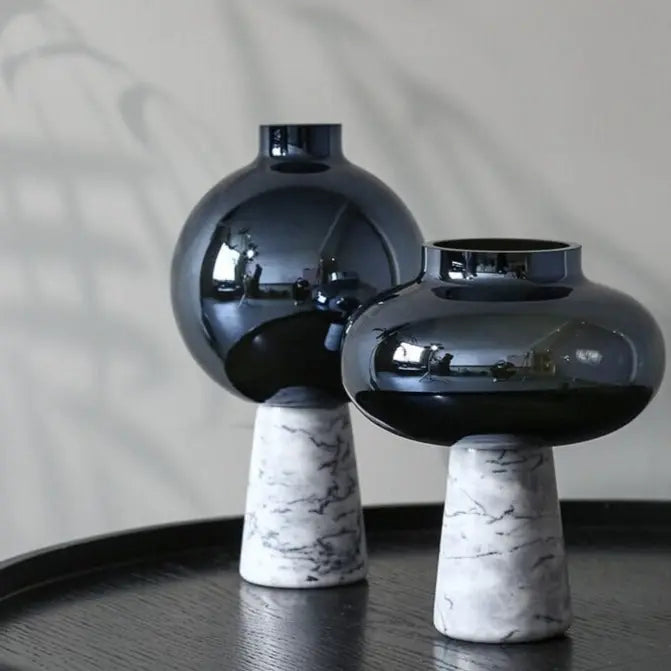 Two black vases with marble bases on a dark surface